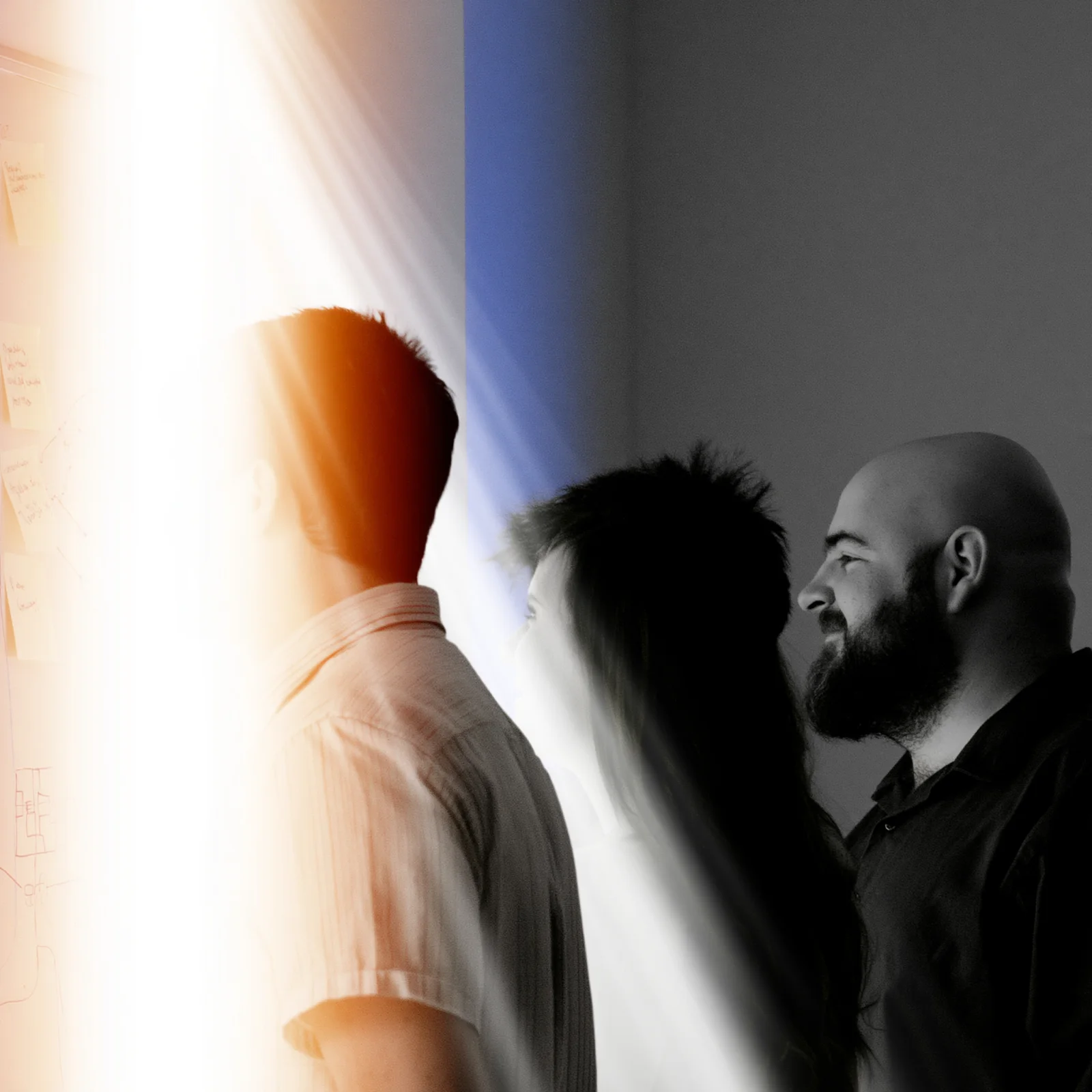 Three people at a planning wall, cut through by a hard prism of orange and blue light